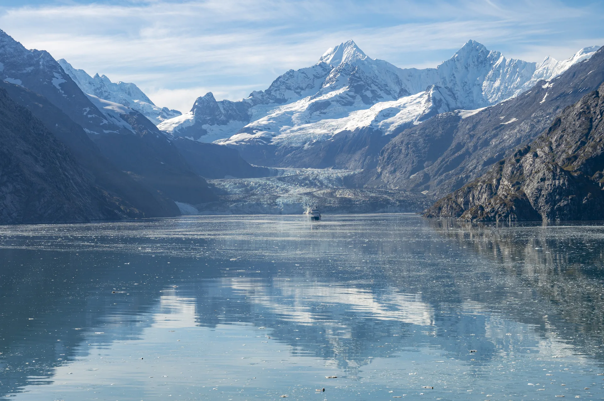 A distant cruise ship below snow-covered peaks and Johns Hopkins Glacier in Glacier Bay, Alaska